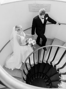 Bride and groom holding hands on elegant spiral staircase, photographed from above in black and white