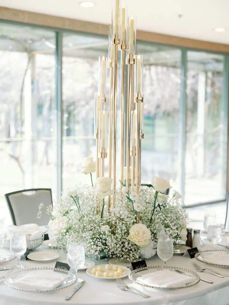 Tall gold candelabra centerpiece with white roses and baby's breath on an elegant reception table with gold-rimmed china