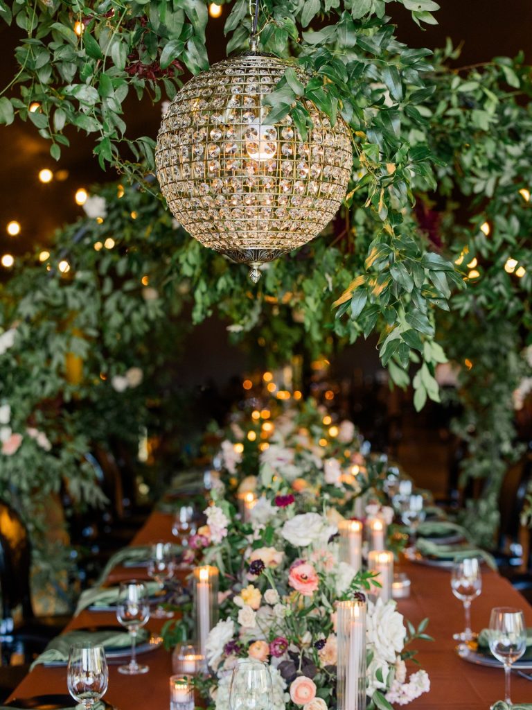 Crystal ball chandelier hanging above elegant reception table with greenery, candles, and colorful floral centerpiece at Jorgensen Farms