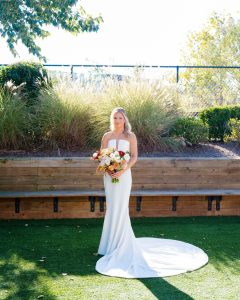 Bride with vibrant fall wedding bouquet featuring burgundy, peach, and cream flowers in garden setting
