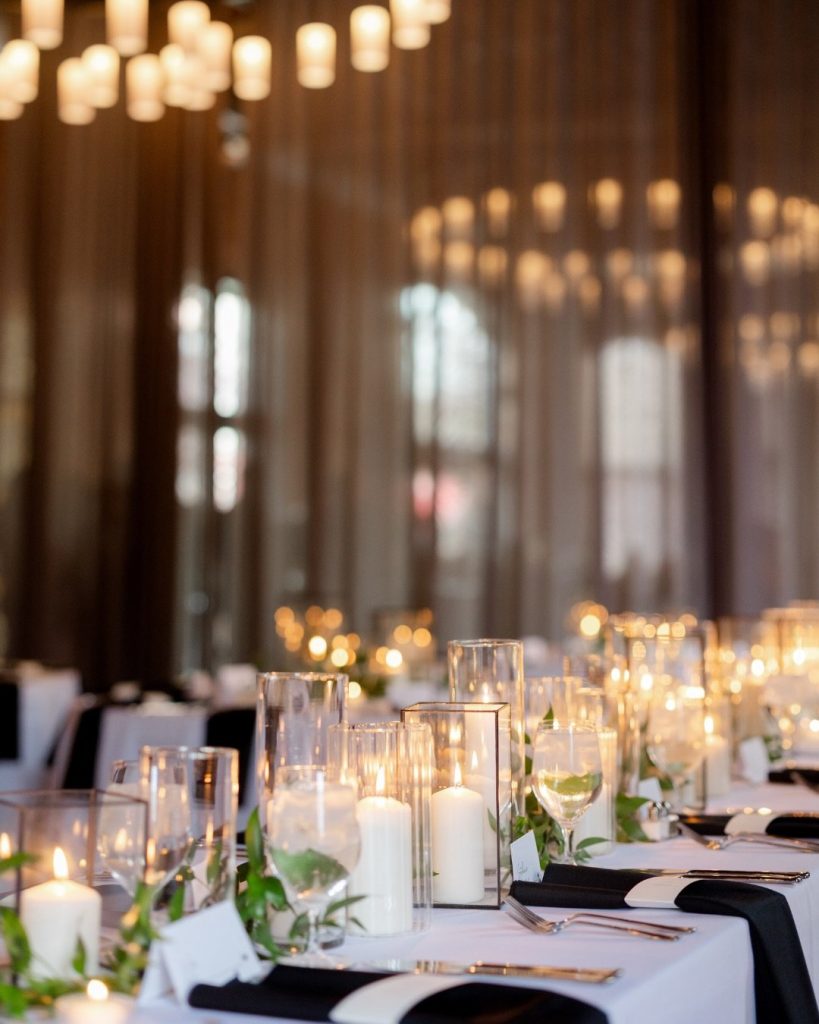 Elegant reception tablescape with pillar candles in glass hurricanes, greenery, and soft candlelight