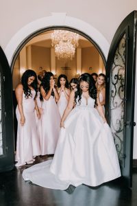 Bride with bridesmaids in pink dresses under arched doorway with chandelier