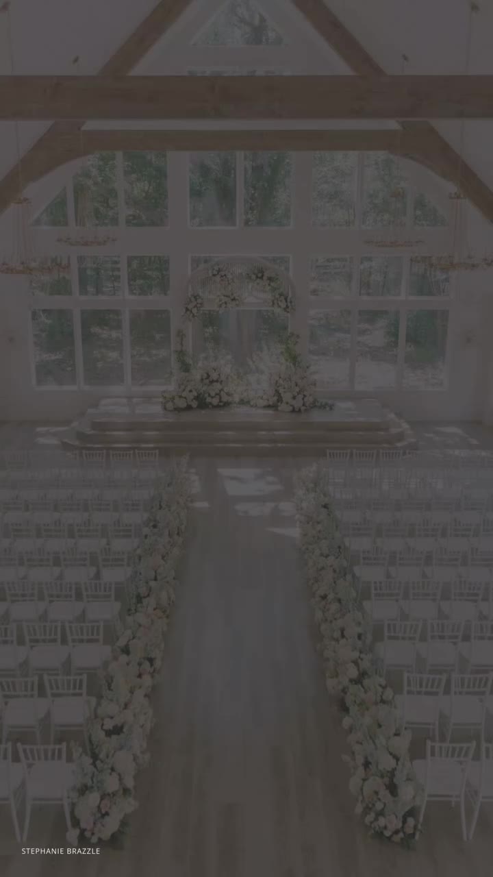 Elegant barn wedding ceremony space with exposed beams, white chiavari chairs, and floral arch altar