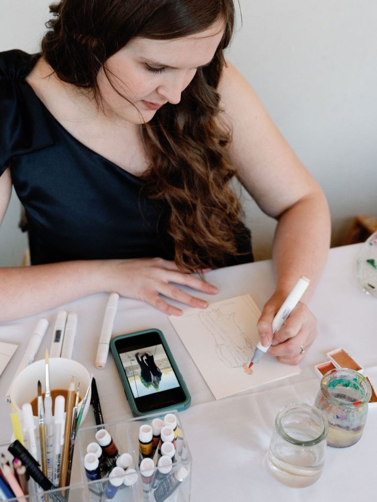 Wedding planner sketching ceremony designs while referencing phone for McKenzi and Alex's celebration