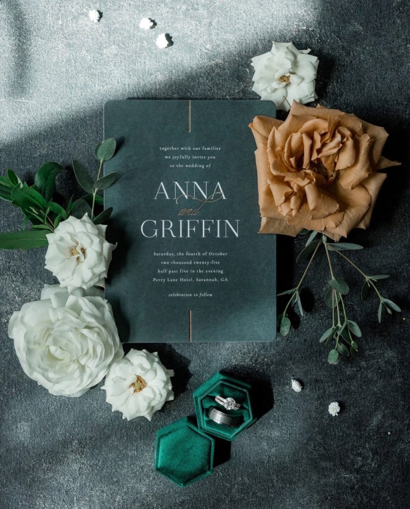 Dark green wedding invitation for Anna and Griffin surrounded by white and caramel roses with emerald ring box