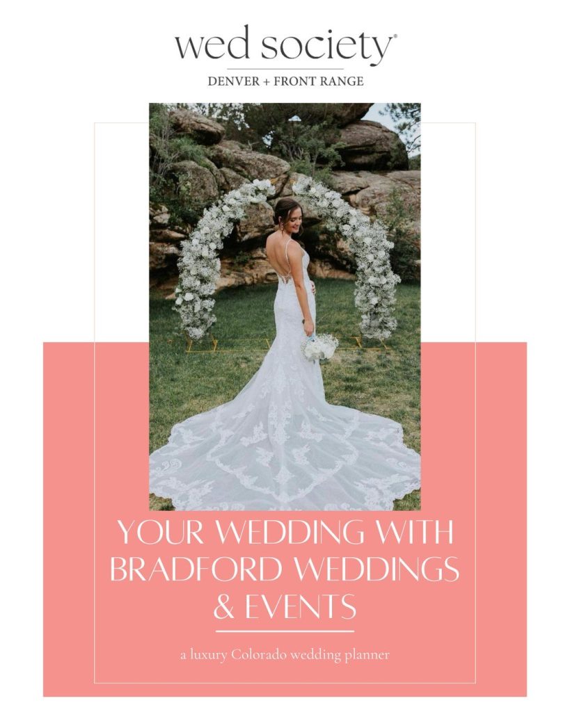 Bride in backless lace wedding gown with long train stands before white floral arch at outdoor Colorado ceremony