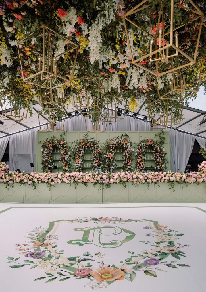Luxury wedding reception with geometric gold chandeliers, lush floral installations, and custom monogram dance floor