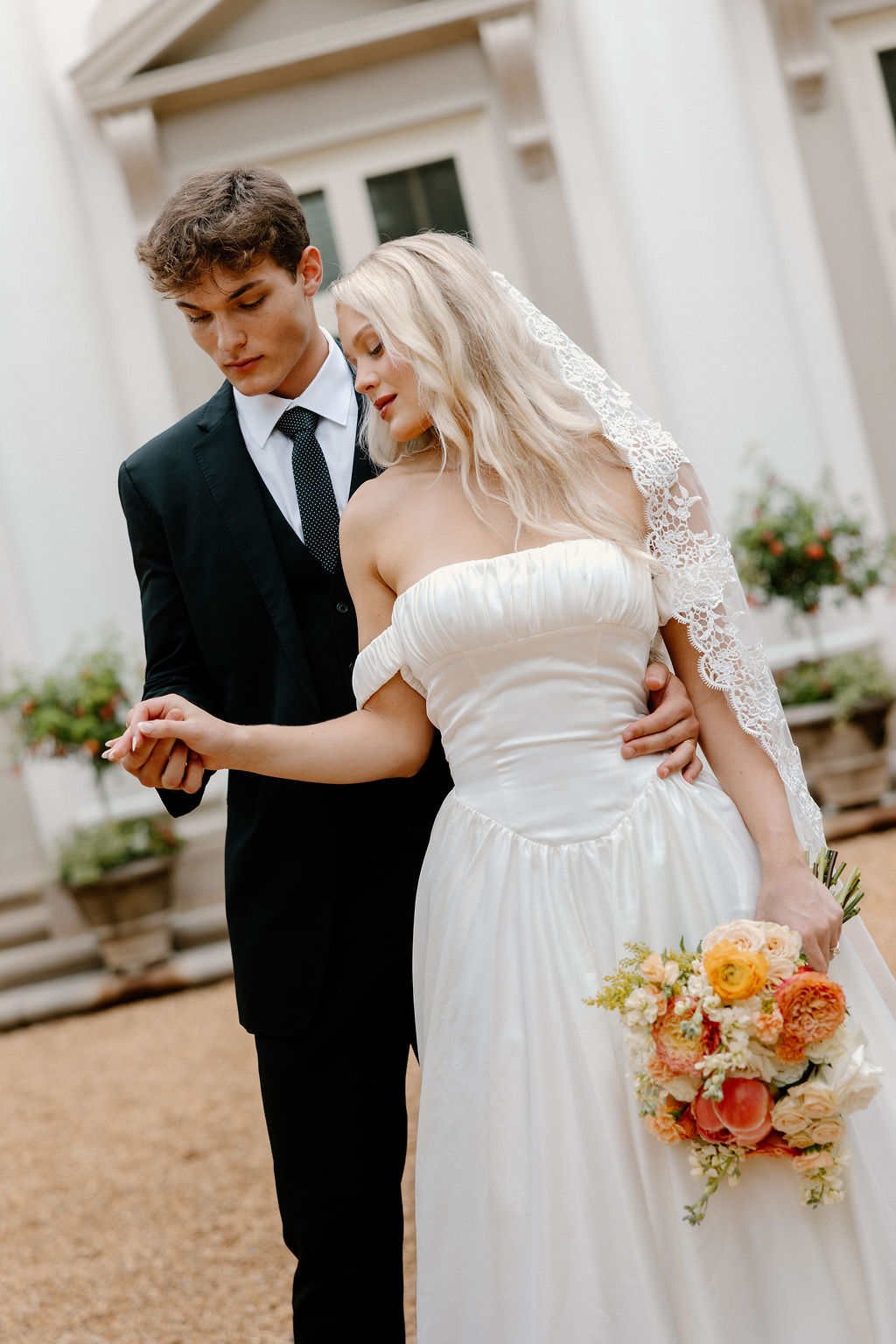 Intimate wedding couple portrait with bride holding colorful spring bouquet in front of white columned building