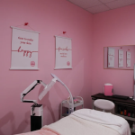 Pink facial treatment room with white massage table and motivational wall art