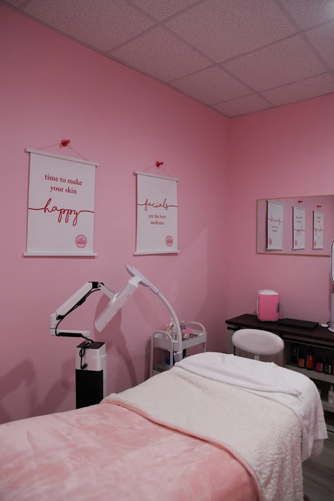 Pink facial treatment room with white massage table and motivational wall art