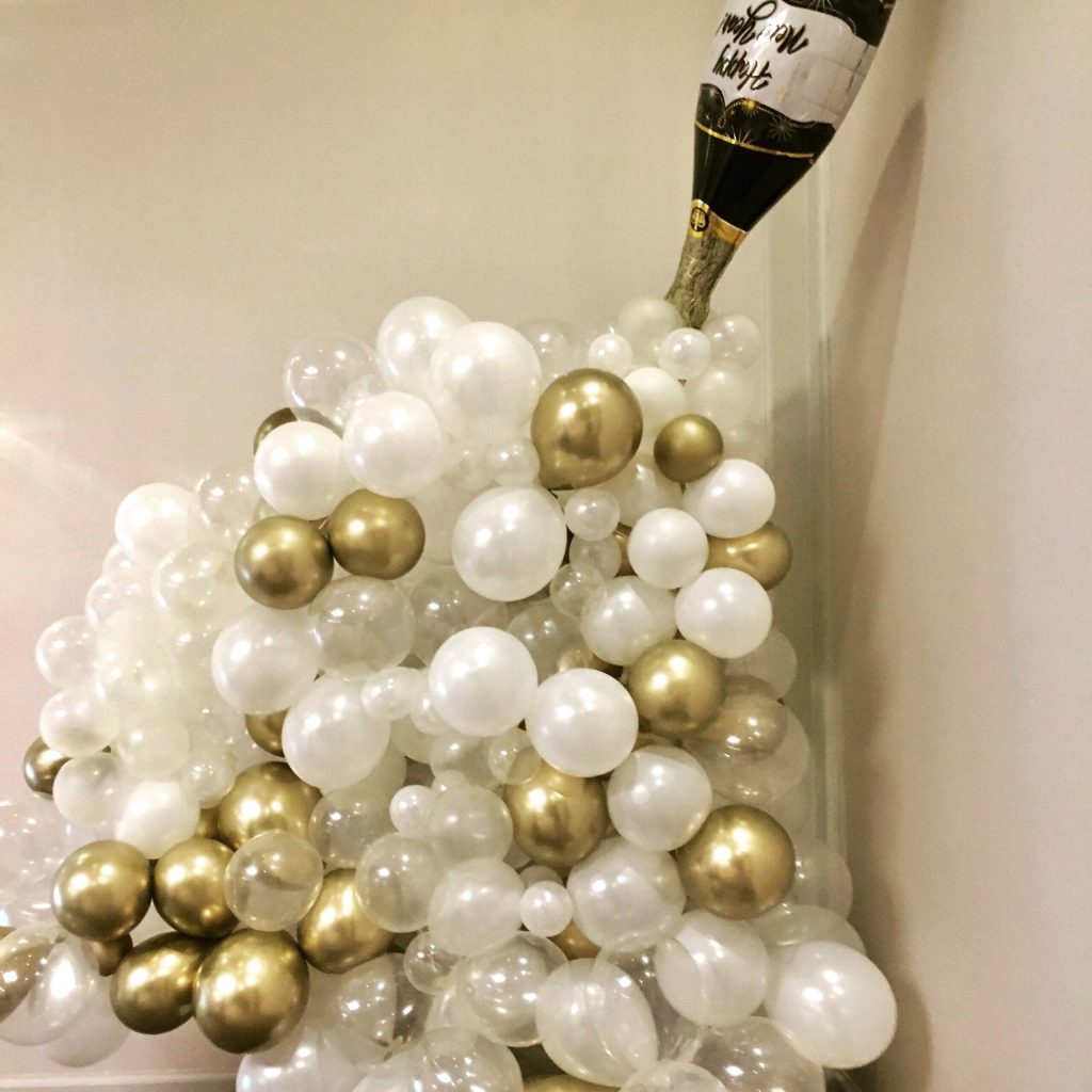 Decorative champagne bottle arrangement with white and gold balloons forming elegant celebratory display
