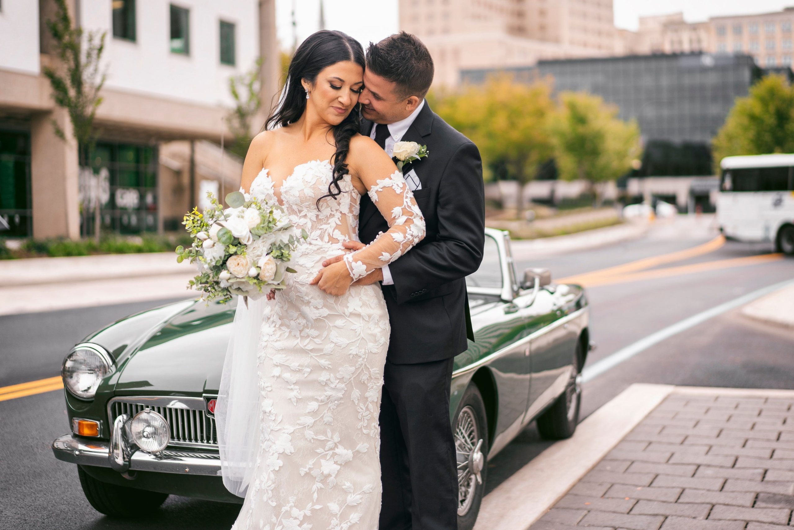 Bride and groom share intimate moment beside vintage green convertible