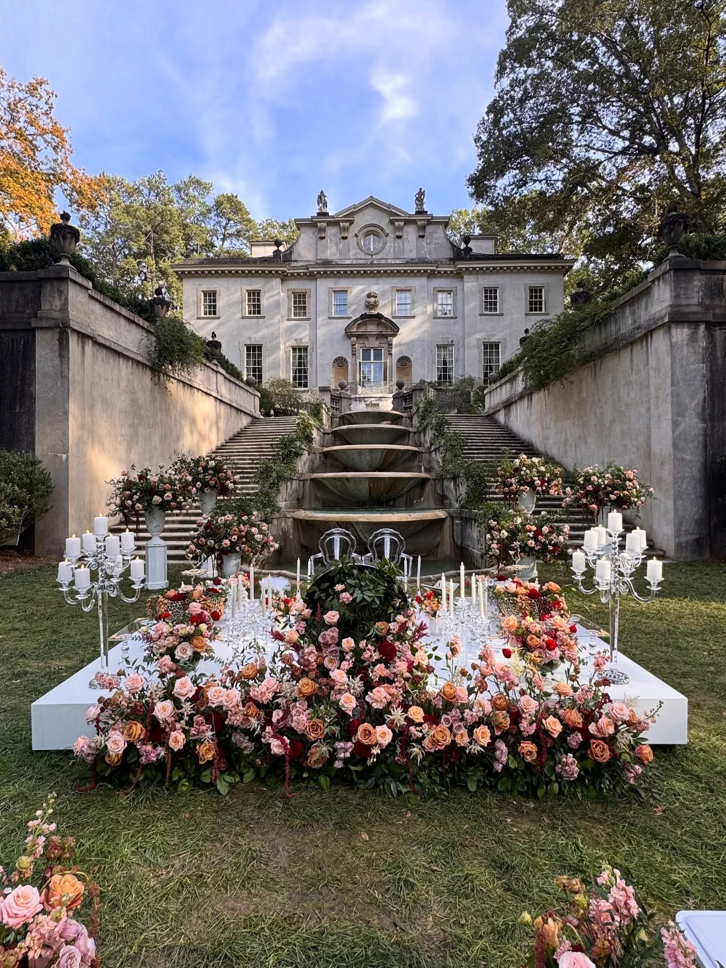 Outdoor Persian wedding ceremony setup with elaborate floral arrangements in coral and pink tones at historic estate venue