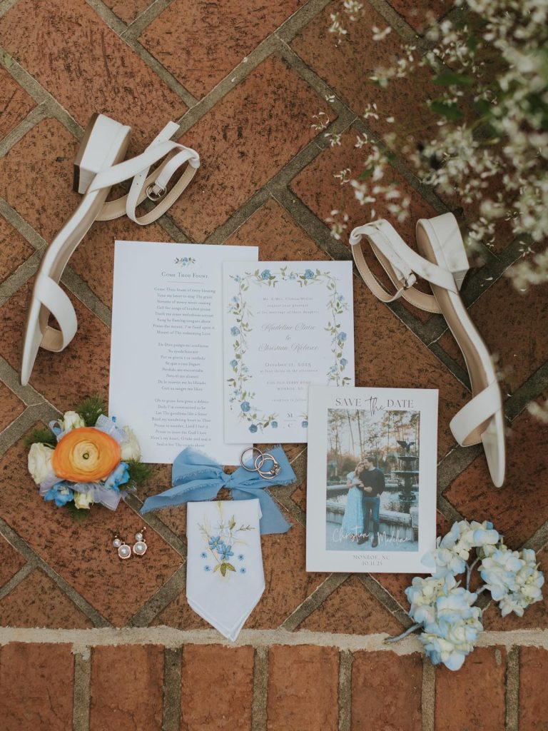 Flat lay of wedding stationery suite with ribbons and floral accents on terracotta surface