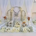 Elegant white Sofreh Aghd setup with circular floral arches, crystal lantern, mirrored table, and white roses