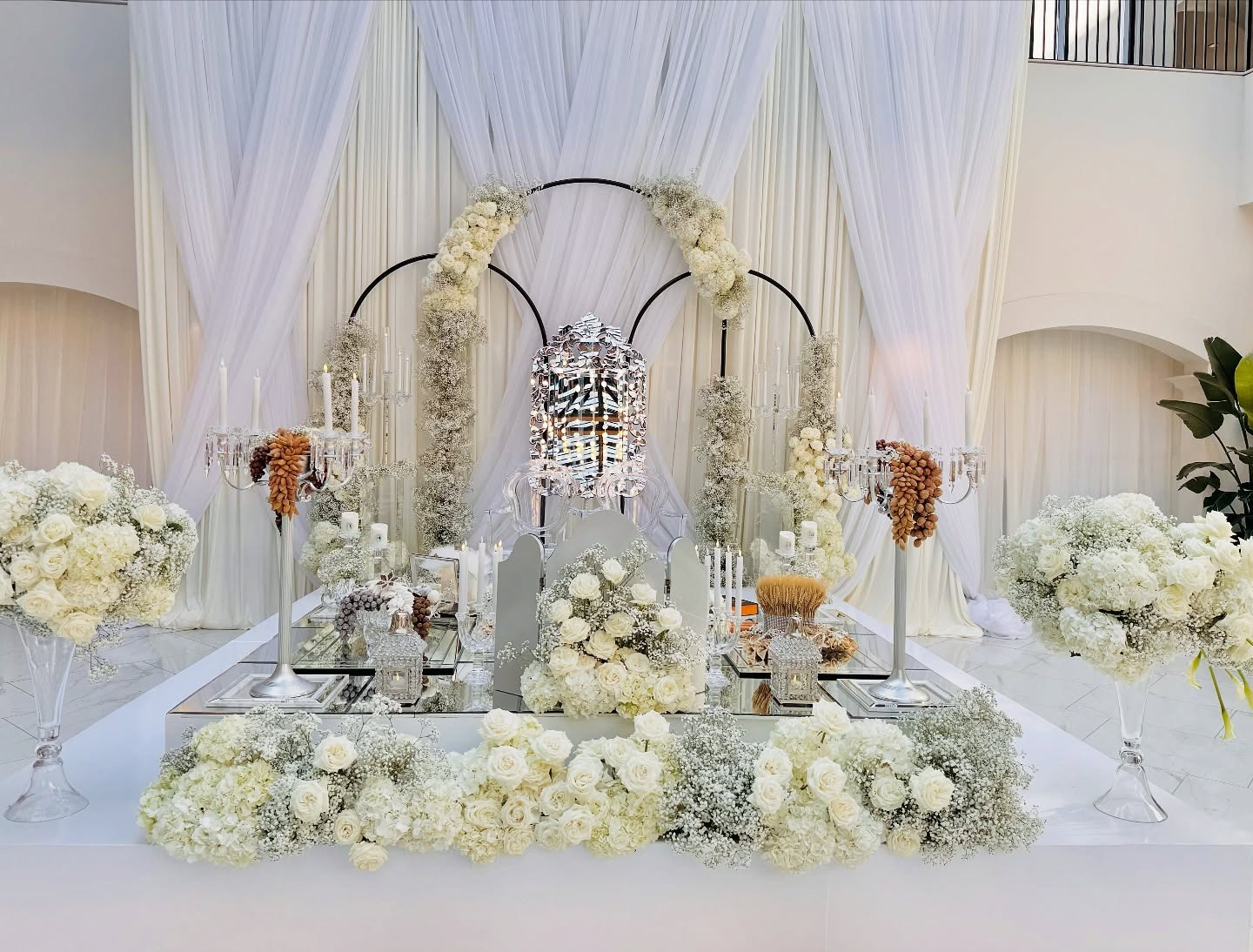 Elegant white Sofreh Aghd setup with circular floral arches, crystal lantern, mirrored table, and white roses