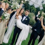 Joyful newlyweds celebrating with wedding party holding white and green floral bouquets outdoors