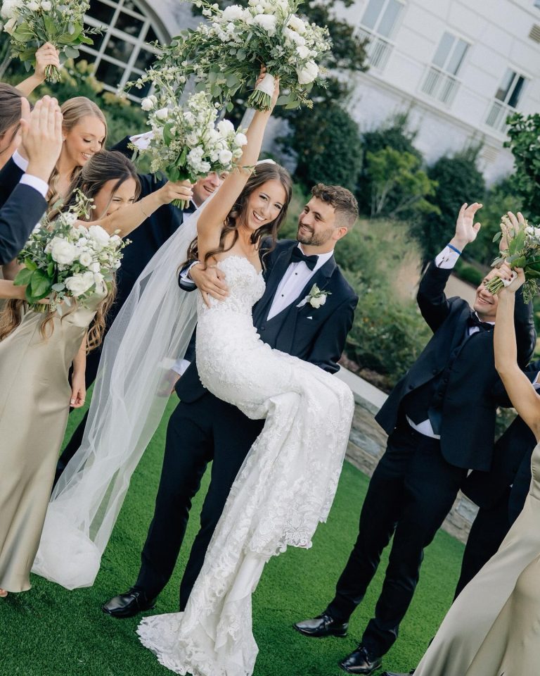 Joyful newlyweds celebrating with wedding party holding white and green floral bouquets outdoors