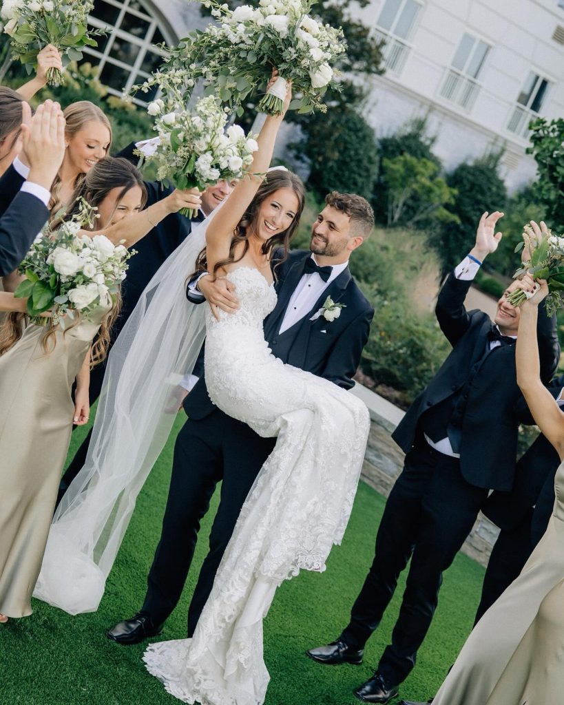 Joyful newlyweds celebrating with wedding party holding white and green floral bouquets outdoors