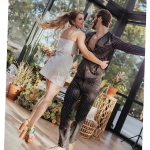 Couple dancing in glass greenhouse venue with floral arrangements and natural light streaming through windows
