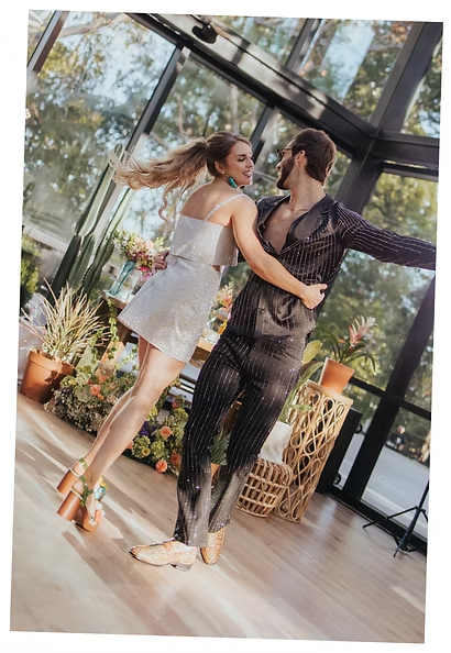 Couple dancing in glass greenhouse venue with floral arrangements and natural light streaming through windows