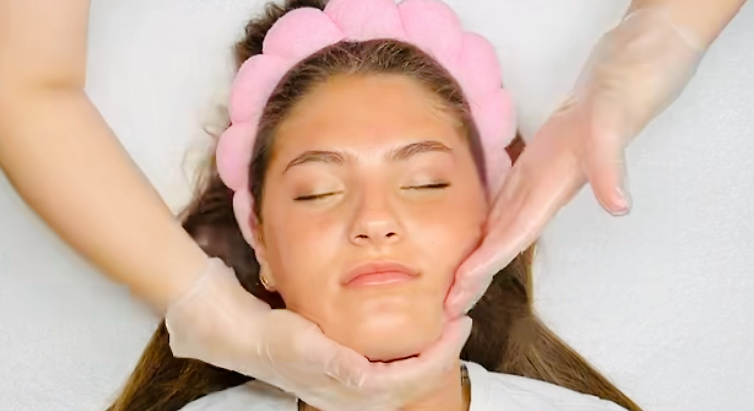 Bride receiving facial massage treatment with pink headband in spa