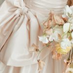 Close-up of blush pink bridesmaid dress with elegant bow sash and pastel floral bouquet