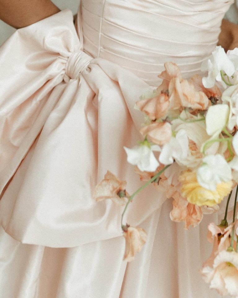 Close-up of blush pink bridesmaid dress with elegant bow sash and pastel floral bouquet