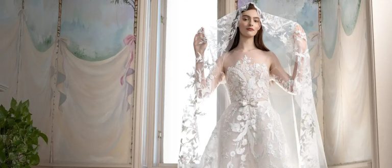 Bride wearing sheer lace wedding gown with elaborate floral appliqués and oversized statement cape sleeves