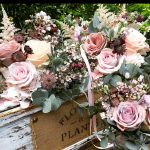 Wedding floral arrangement with blush roses, burgundy accents, and eucalyptus in rustic container with "thank you" tag