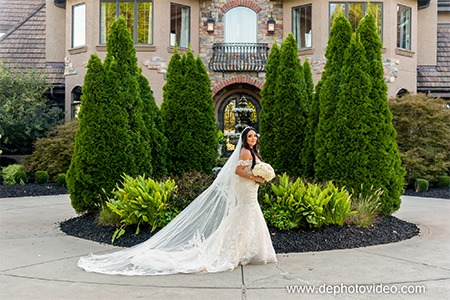 Bride in flowing veil posing at elegant estate with manicured landscaping