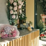 Wedding stationery display area with gold bar, pink florals, and romantic rose wall backdrop