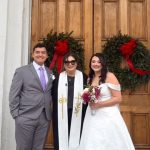 Reverend Susie with newlyweds in front of church doors decorated with holiday wreaths