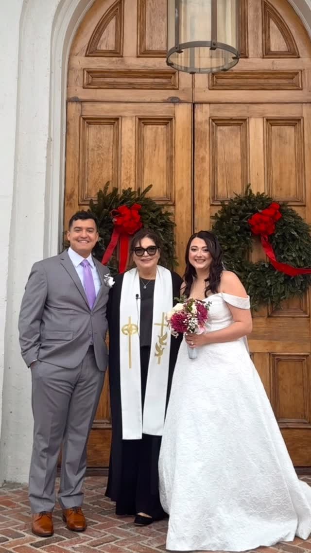 Reverend Susie with newlyweds in front of church doors decorated with holiday wreaths