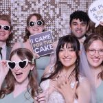 Wedding party posing with props in photo booth with sequin backdrop, bride showing engagement ring