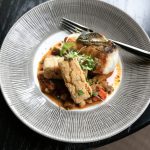 Seared scallops with microgreens and crispy bread on textured white plate