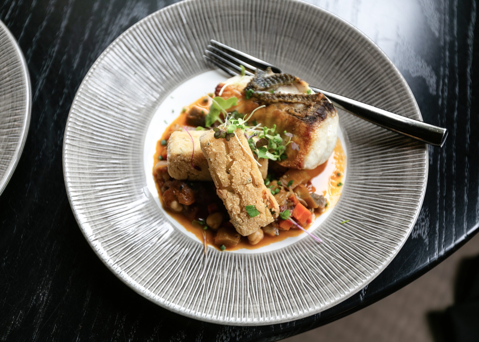 Seared scallops with microgreens and crispy bread on textured white plate