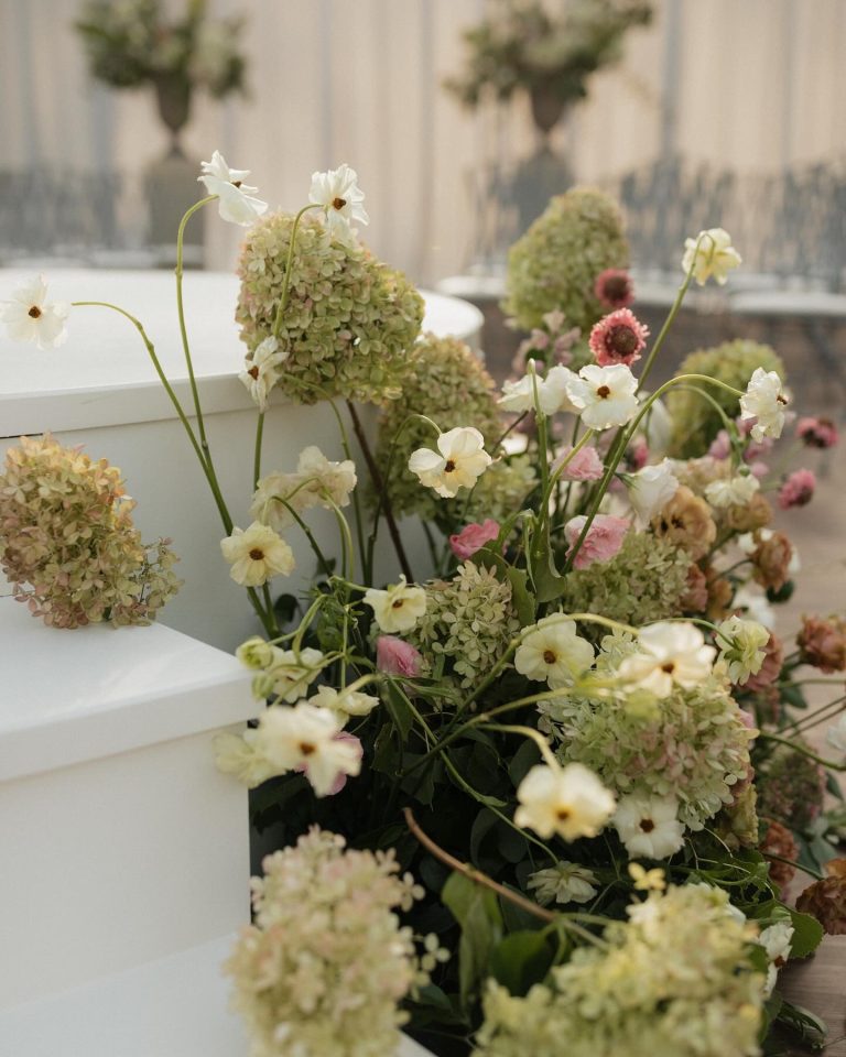 Garden-style arrangement of white cosmos, green hydrangeas, and pink flowers on white marble steps