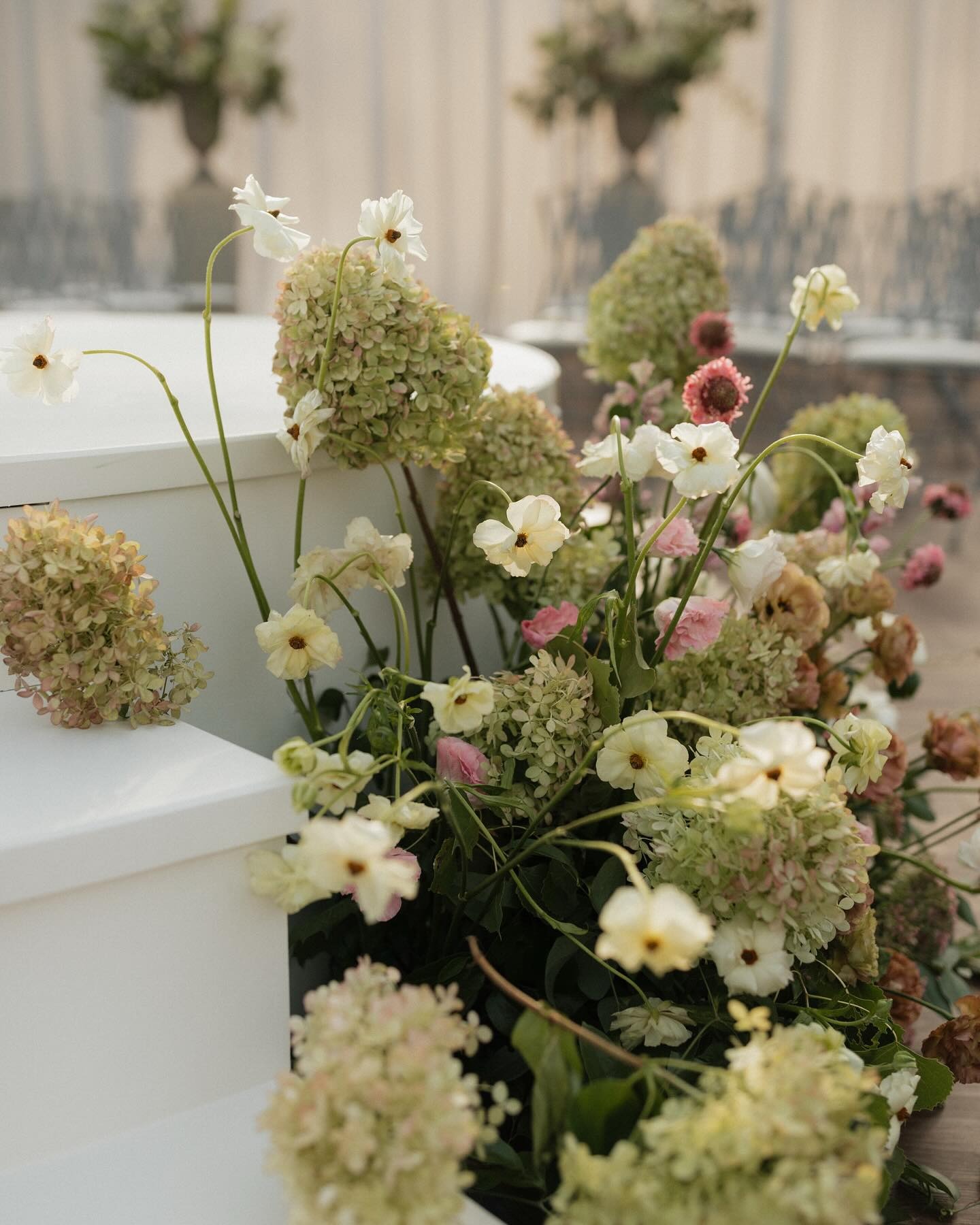 Garden-style arrangement of white cosmos, green hydrangeas, and pink flowers on white marble steps