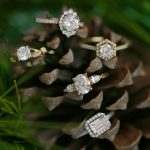 Collection of five diamond engagement rings in gold and rose gold arranged on rustic pine cone
