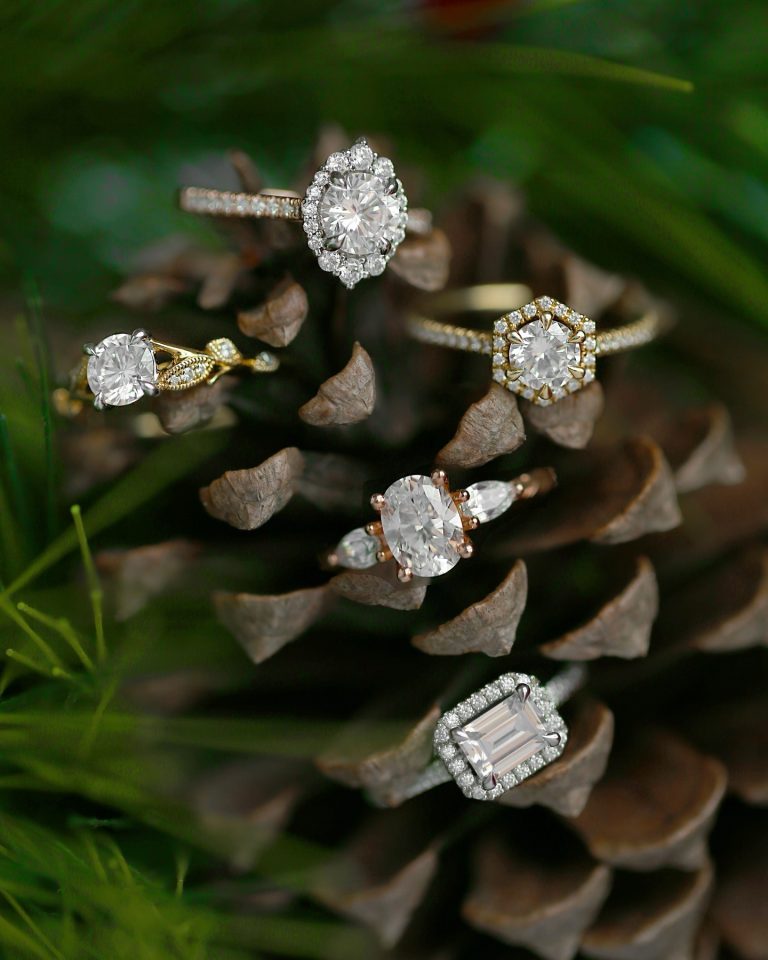 Collection of five diamond engagement rings in gold and rose gold arranged on rustic pine cone