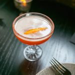 Layered craft cocktail with citrus garnish and votive candle on marble table