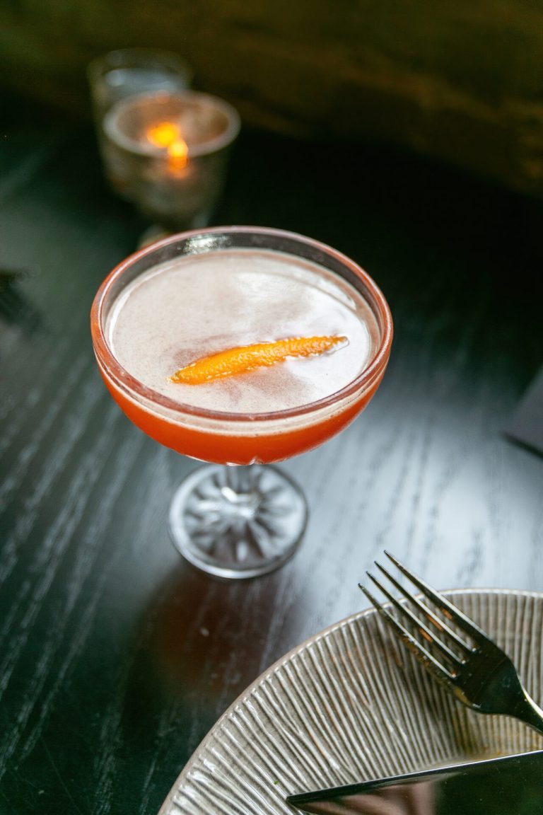 Layered craft cocktail with citrus garnish and votive candle on marble table