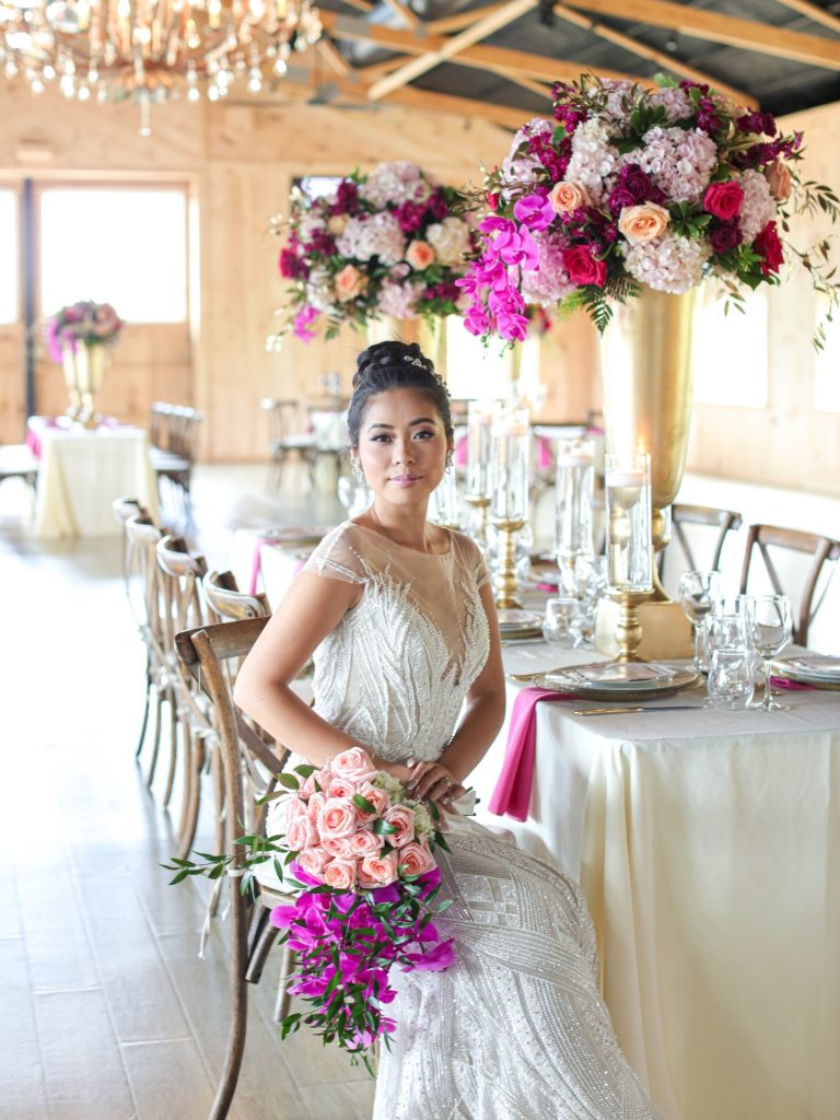 Bride sitting down during indoor wedding reception. Wedding flowers are pink and mauve color. white reception decor