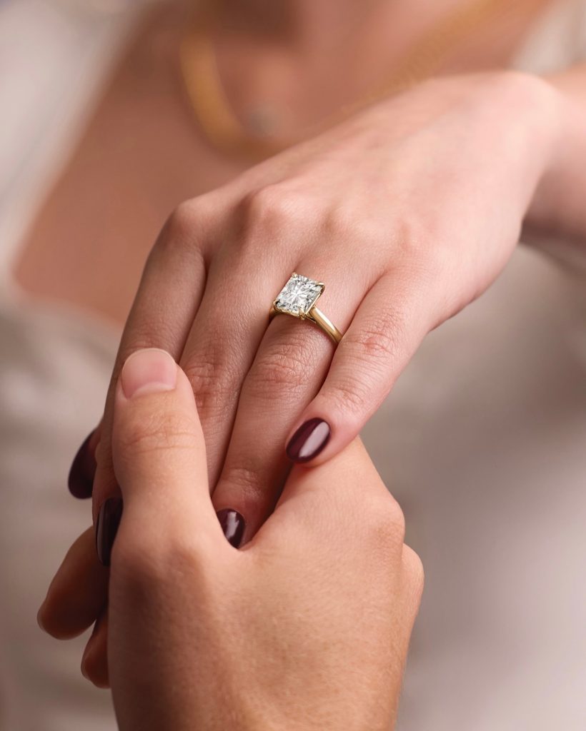 Emerald-cut diamond engagement ring with gold band worn on woman's hand