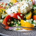 Herb-crusted fish fillet with roasted peppers and corn succotash on textured white plate
