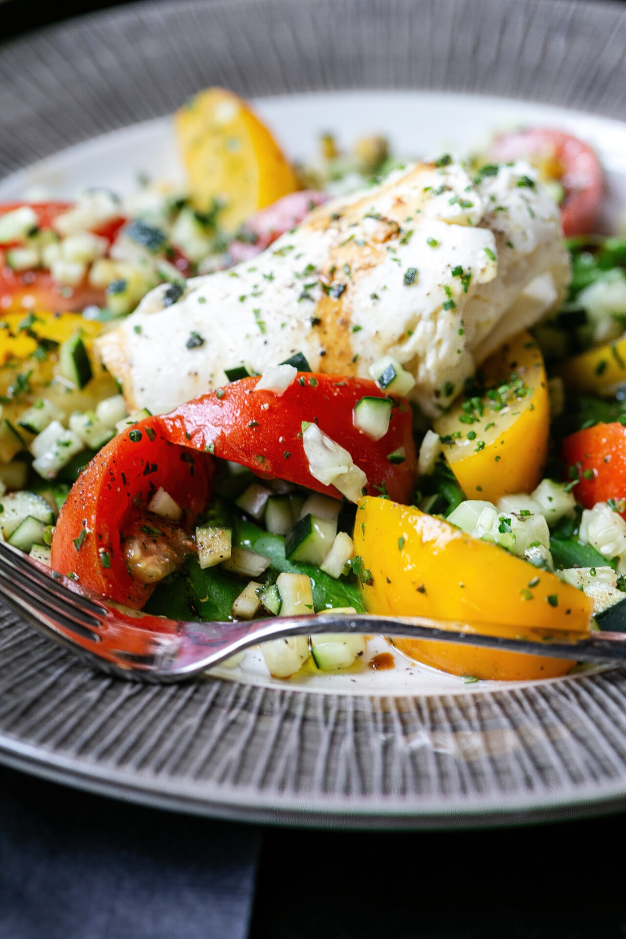 Herb-crusted fish fillet with roasted peppers and corn succotash on textured white plate
