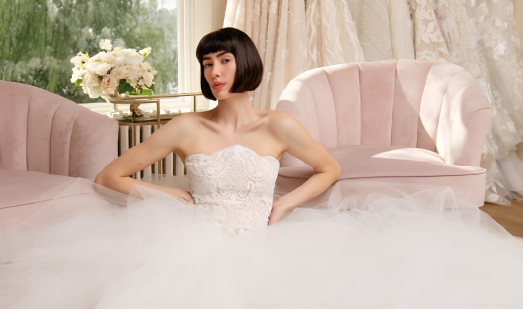 Bride in strapless beaded bodice gown with voluminous tulle skirt seated in elegant bridal boutique