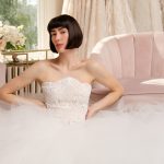 Bride in strapless beaded bodice gown with voluminous tulle skirt seated in elegant bridal boutique