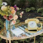 Vintage gold mirrored tray displaying colorful dahlia and anemone bouquet beside yellow rotary phone and wedding guestbook